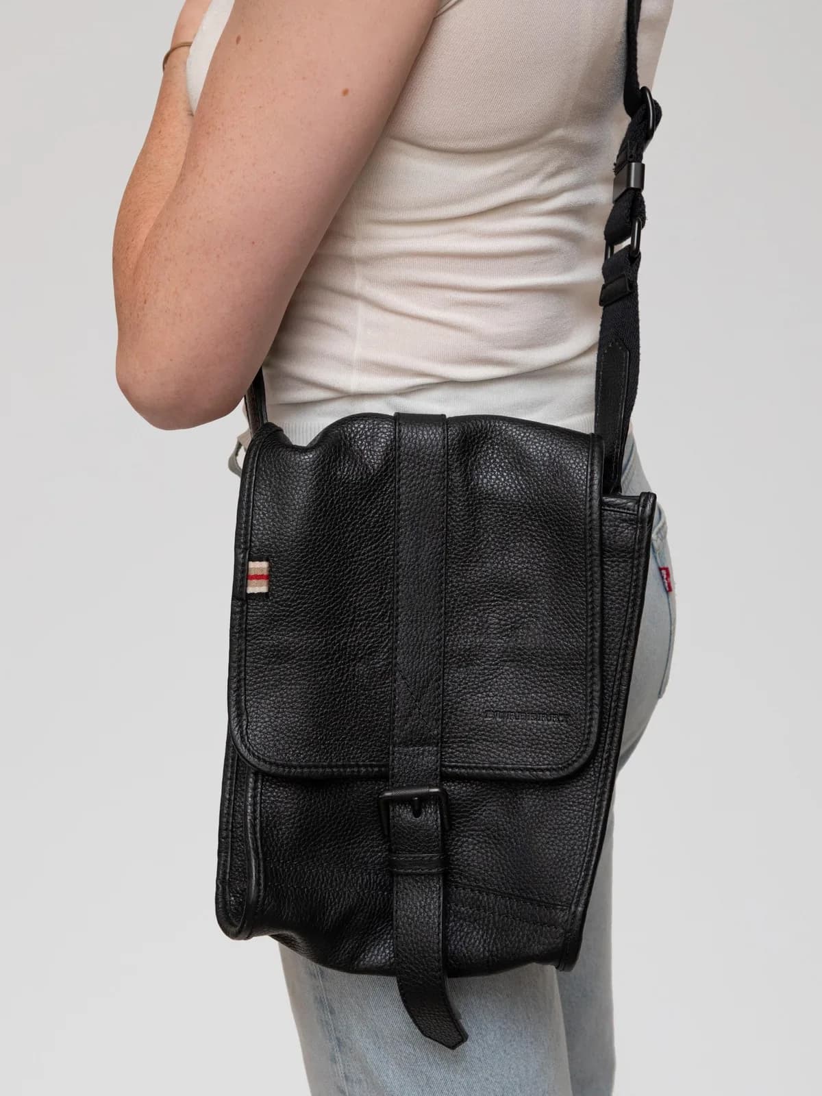 Crafted from supple black grain leather with a buckled flap and subtle stripe accent, this vintage Burberry messenger bag reveals a classic check-lined interior for understated, functional luxury. - Image 1
