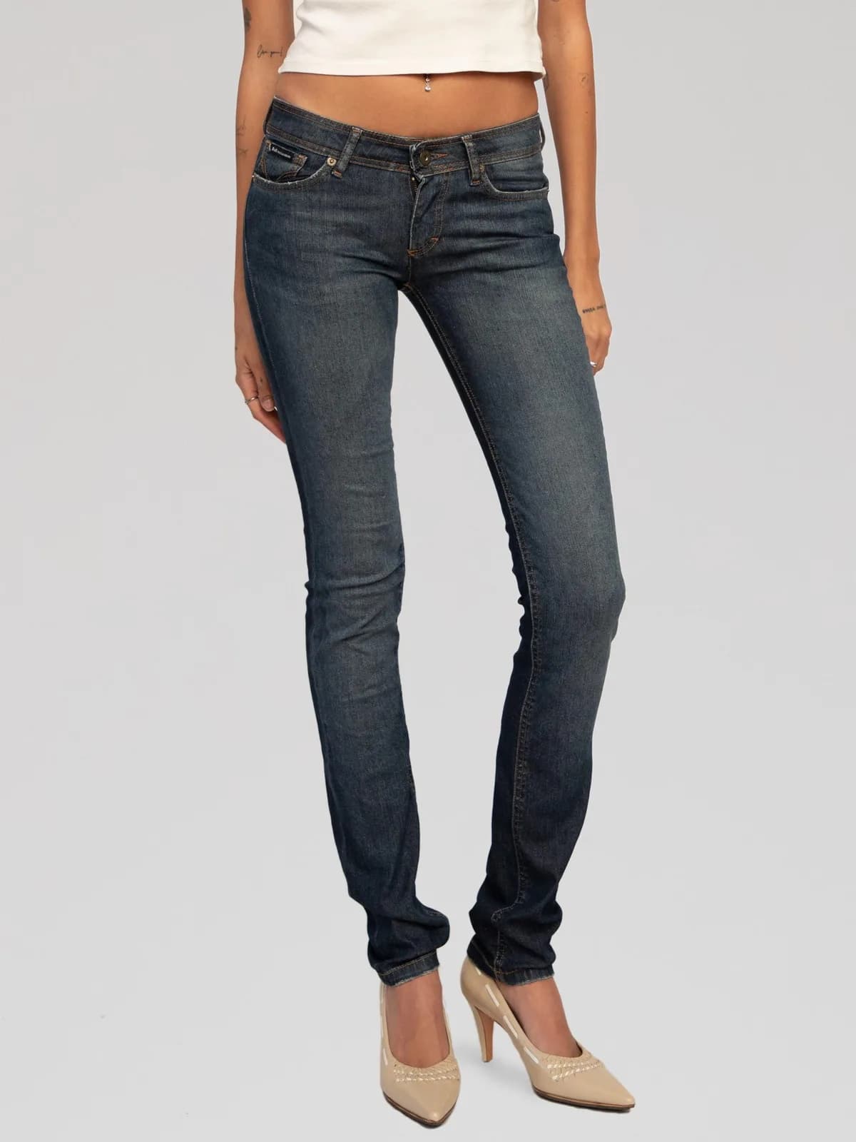 D&G Dolce & Gabbana low-rise slim-fit jeans crafted in dark wash blue stretch denim with subtle whiskering and fading. Features classic five-pocket styling, contrast yellow topstitching, belt loops, and a zip fly with button closure. Finished with a signature metal logo plaque patch on the back right pocket. Made in Italy. - Image 1