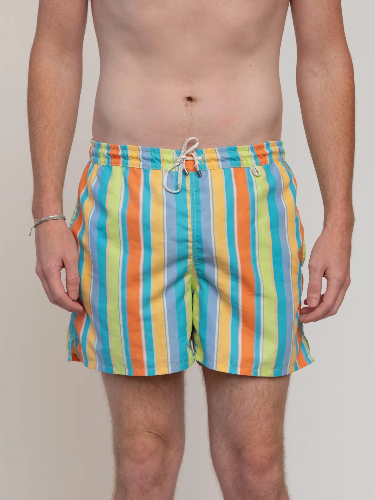 Loro Piana swim trunks featuring vibrant vertical multi-colored stripes in shades of turquoise, orange, yellow, lime green, and cornflower blue. Crafted from lightweight quick-dry technical fabric, designed with an elasticated drawstring waistband with silver-tone hardware tips, side slip pockets, a rear flap pocket, and a supportive inner mesh lining. Made in Italy. - Image 1