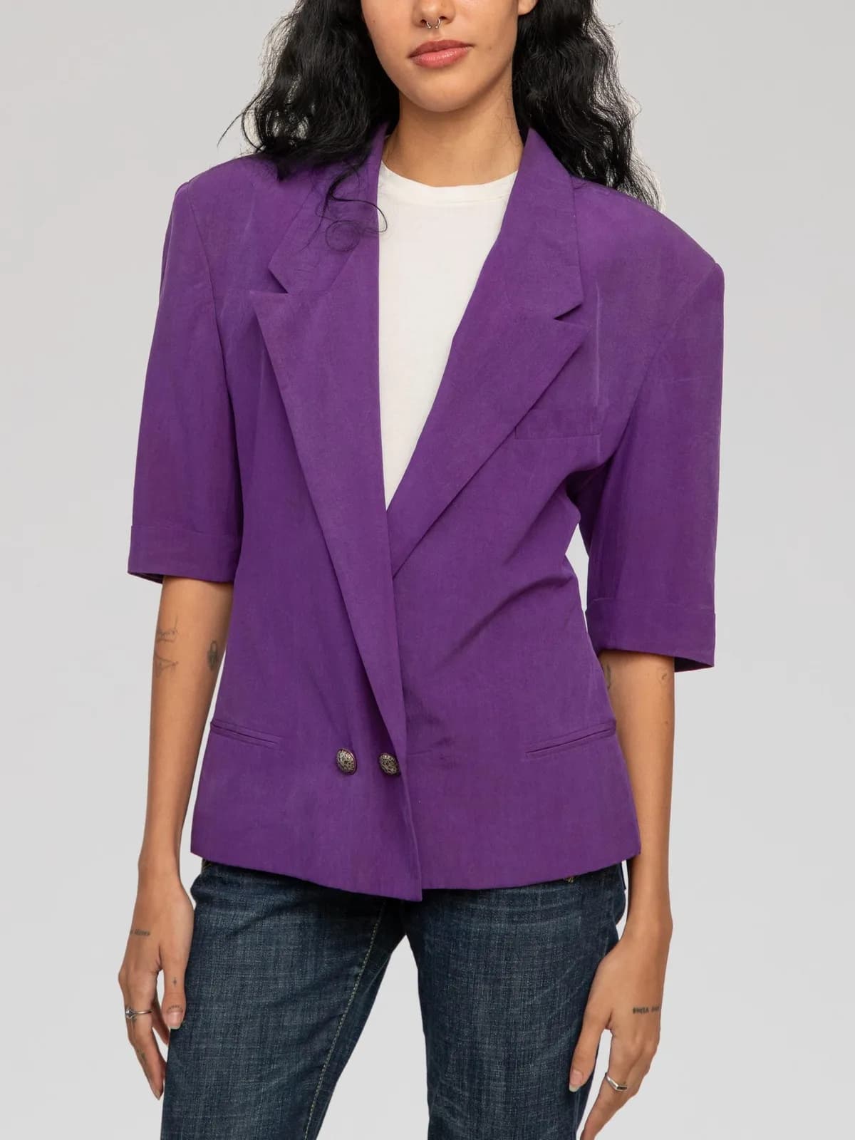 Versus Gianni Versace vivid purple short-sleeve blazer featuring wide notch lapels, structured padded shoulders, a low double-breasted two-button closure with decorative metallic buttons, front welt pockets, chest slip pocket, and elbow-length cuffed sleeves. Crafted in Italy from 100% silk. - Image 1