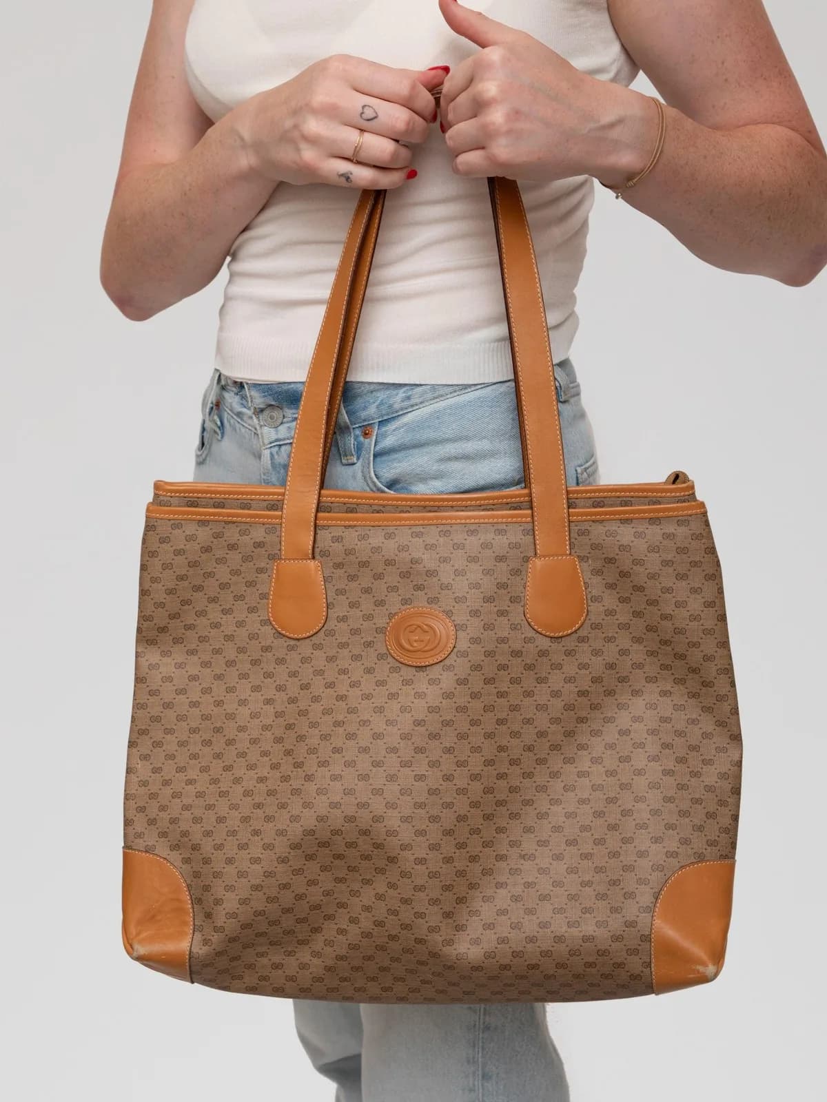 Crafted in classic micro-GG canvas with warm cognac leather handles and trim, this spacious vintage Gucci tote features a centered interlocking GG leather emblem for an elegant, timeless touch. - Image 1