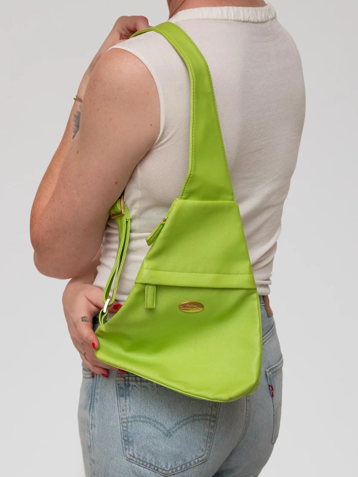 Rendered in a vibrant chartreuse green hue, this vintage Parfums Christian Dior sling bag features an asymmetrical triangular silhouette, front zip compartment, and an oval gold-tone logo plaque for a striking pop-of-color statement. - Image 1