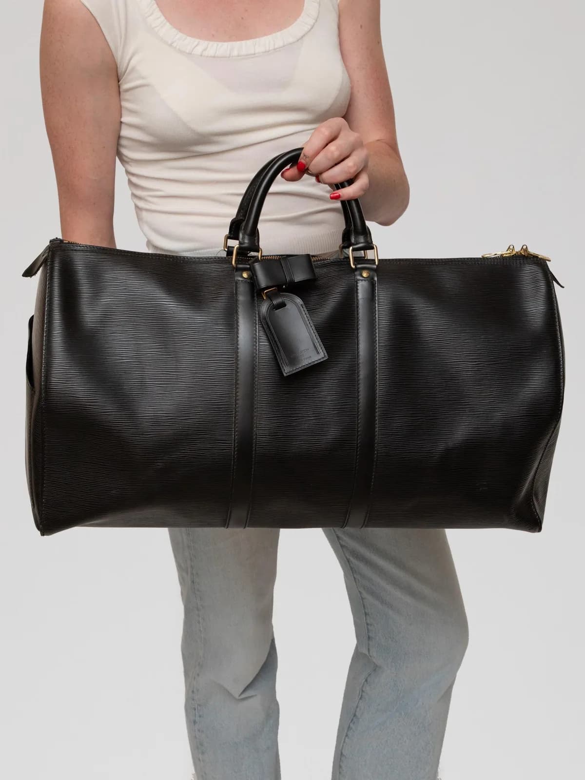 Crafted in durable Noir Epi leather with rich brass hardware, this iconic vintage Louis Vuitton Keepall 50 duffle bag features sturdy rounded leather top handles, an exterior side slip pocket, a double zip closure, and a matching leather ID tag for timeless travel luxury. - Image 1