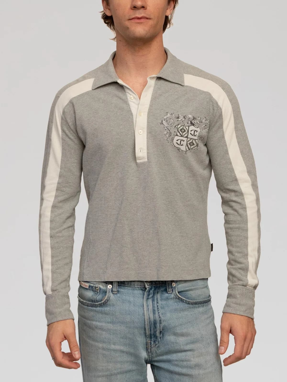 Just Cavalli long-sleeve polo shirt crafted in light grey cotton piqué fabric. Features contrast off-white racing stripes down the raglan sleeves, an off-white partial button placket with a spread collar, single-button barrel cuffs, and a straight hem. Detailed with a vintage-style graphic coat-of-arms crest embroidered on the left chest. Made in Italy. - Image 1