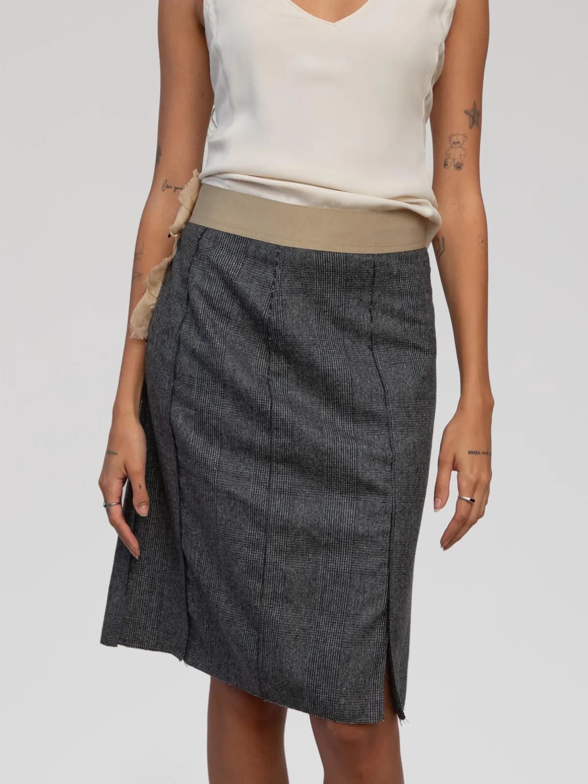 Vintage D&G Dolce & Gabbana knee-length pencil skirt in a charcoal grey Prince of Wales plaid wool weave. Features a contrasting beige grosgrain elasticated waistband, exposed contrast seam details, side hem slits, and a prominent side zip closure trimmed with raw-edge ruffled chiffon fabric. - Image 1