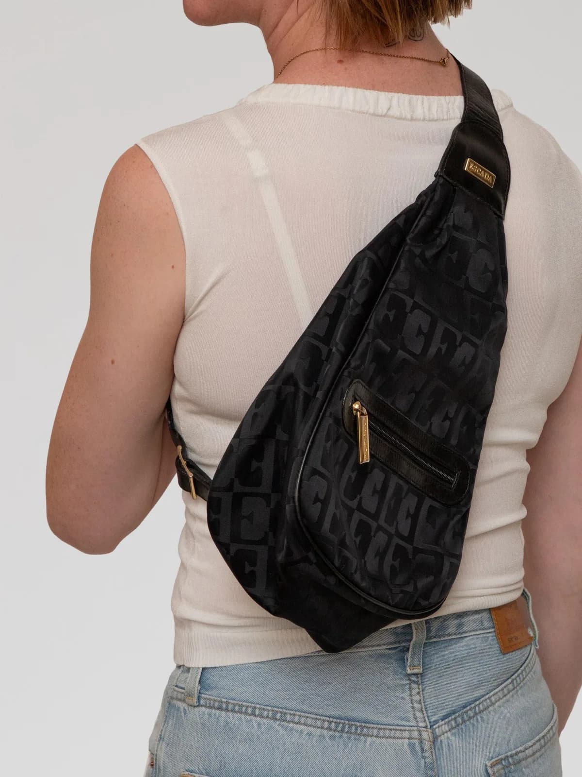 Crafted in sleek black monogram jacquard fabric with polished gold-tone hardware, this vintage Escada sling backpack features an ergonomic teardrop silhouette, a handy front zip pocket, and an adjustable leather strap for a chic, hands-free modern look. - Image 1