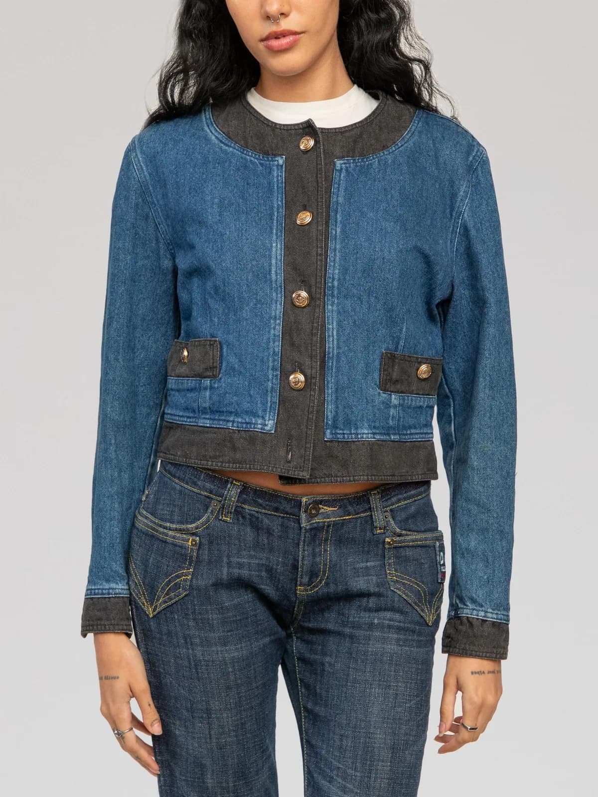 Two-tone Moschino denim jacket featuring a collarless round neckline, contrast dark grey washed denim trim along the placket, collar, hem, and cuffs, dual front flap pockets with gold-tone branded buttons, a button-down front closure, and buttoned sleeve cuffs. - Image 1