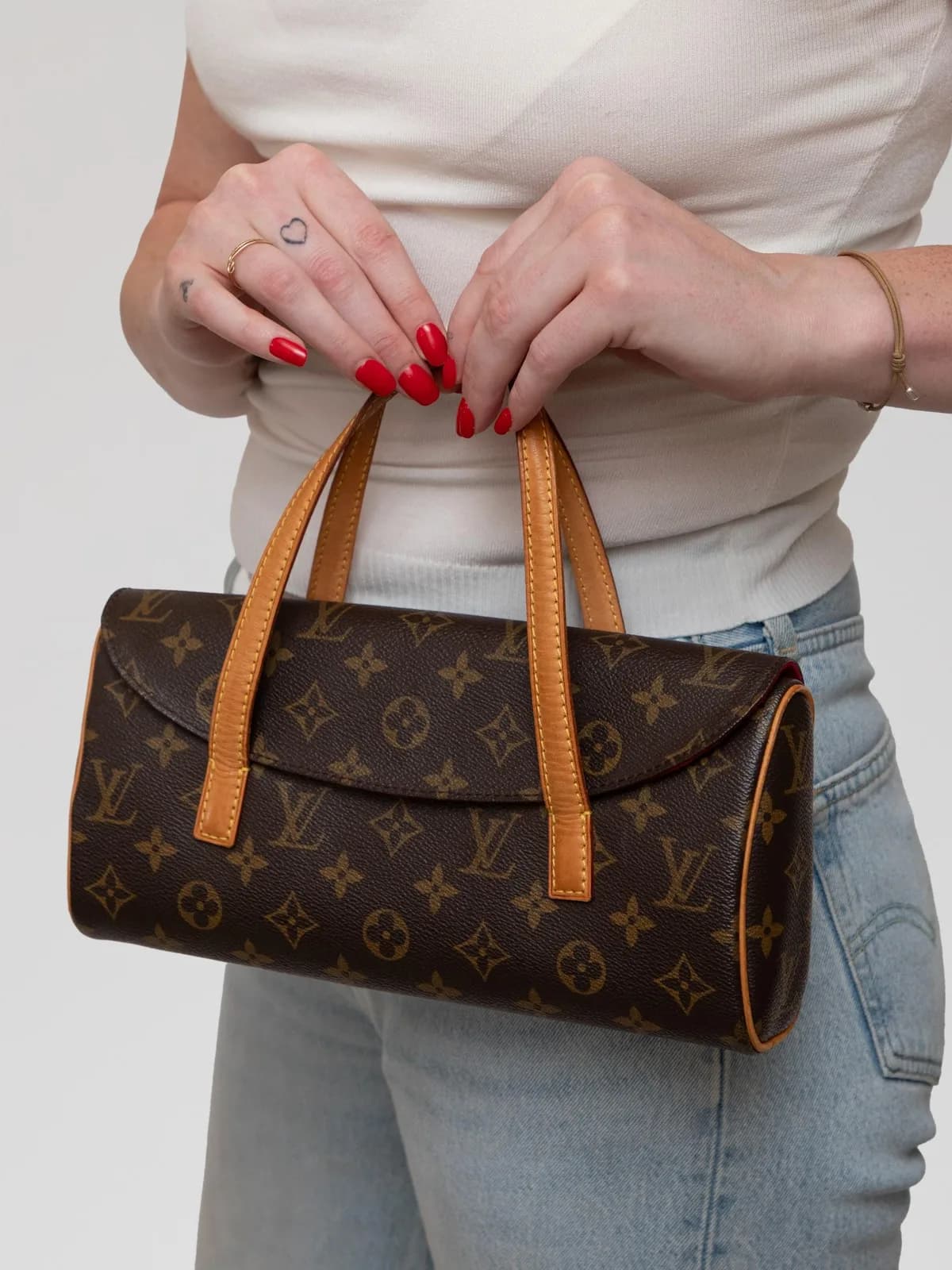 Crafted in iconic Monogram canvas with natural cowhide leather trim, this classic Louis Vuitton Sonatine handbag opens to reveal a luxurious crimson microfiber lining, offering an elegant blend of timeless heritage and effortless sophistication. - Image 1