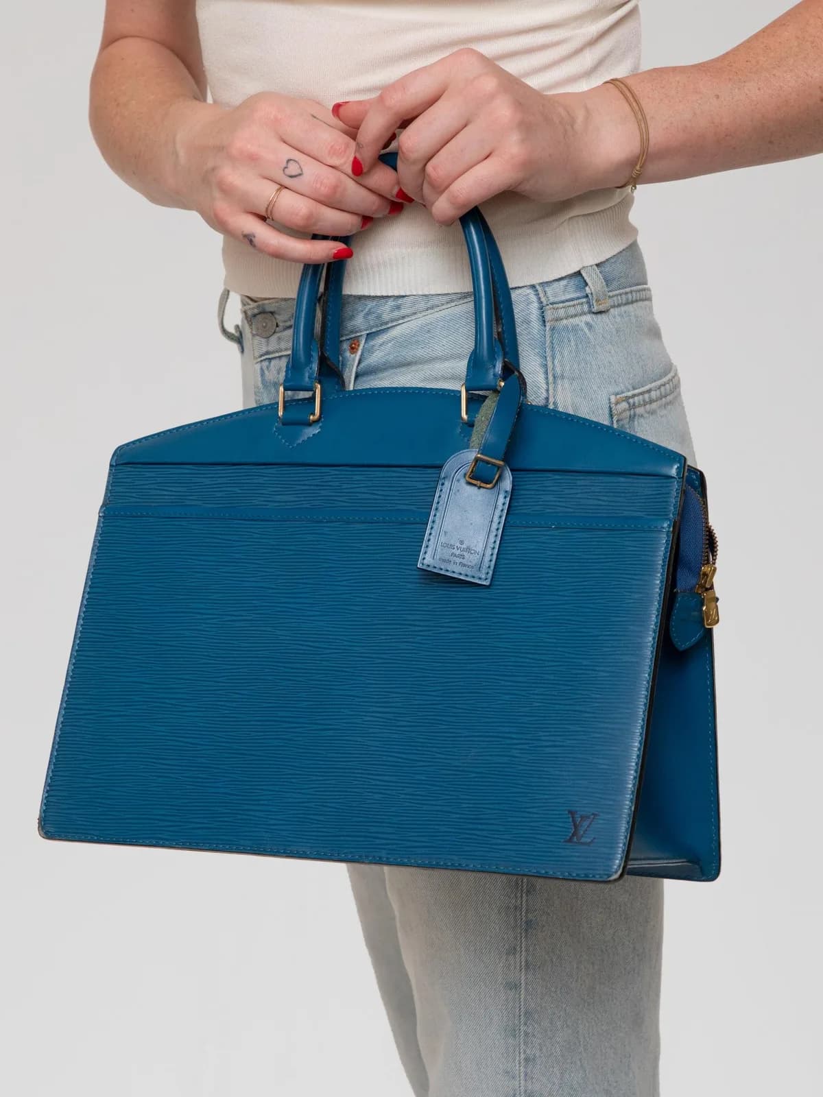 Crafted from vibrant Toledo Blue Epi leather, this vintage Louis Vuitton Riviera handbag features a structured trapezoidal silhouette with dual rolled top handles, an exterior slip pocket, a matching leather luggage tag, and a subtle debossed LV logo signature. - Image 1