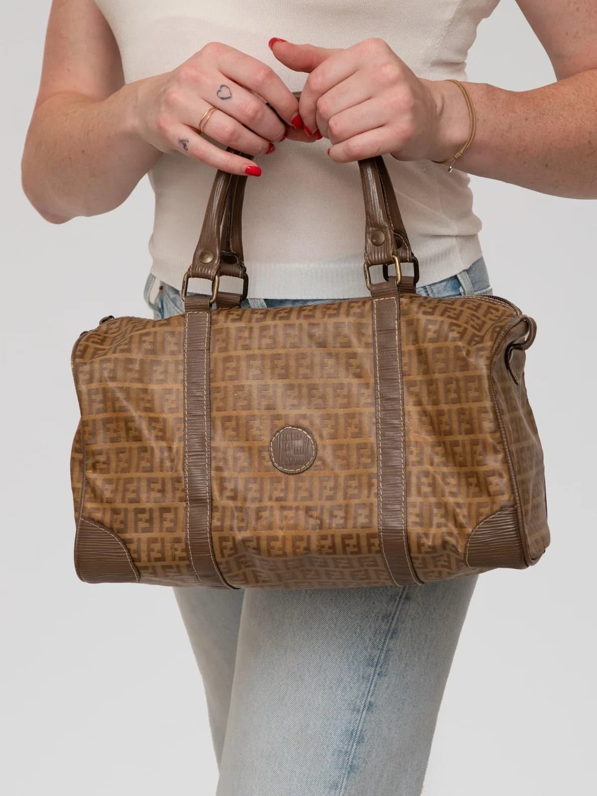 Crafted in warm brown coated canvas with an all-over micro FF logo print, this vintage Fendi Boston bag features structured top handles, textured leather trim, and an embossed circular logo patch for an unmistakable nod to Italian logomania. - Image 1