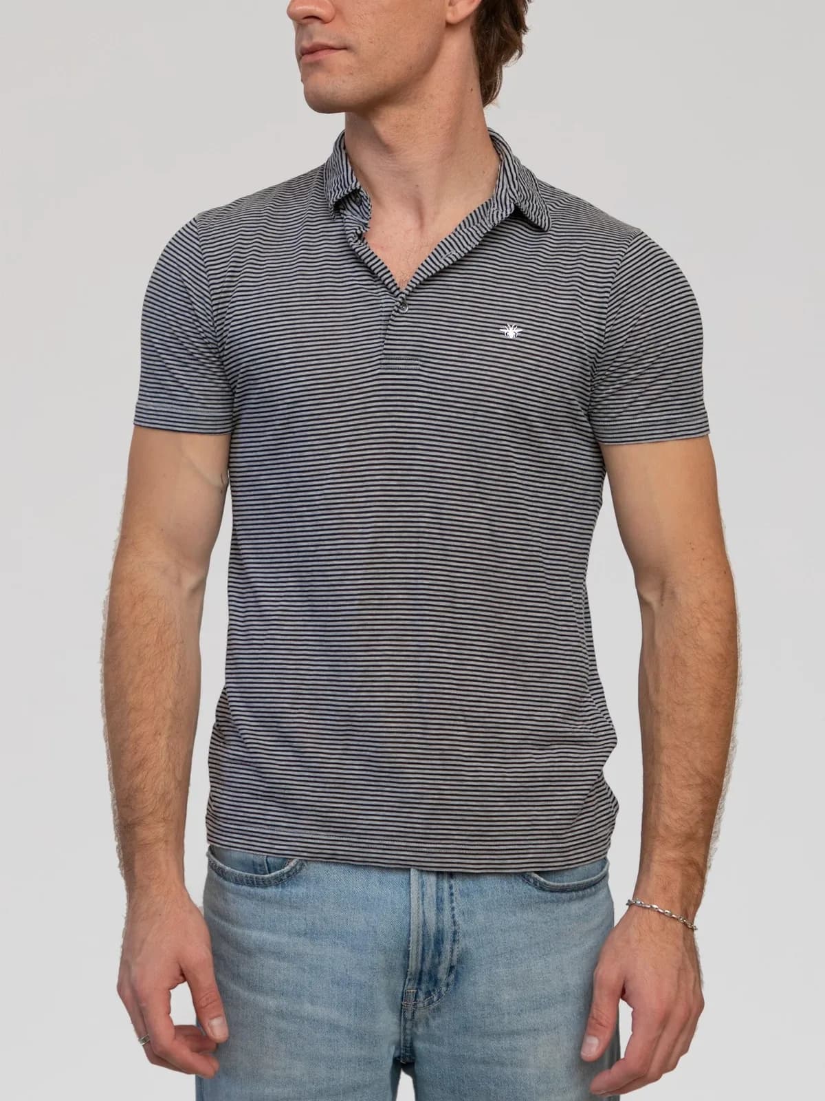Hedi Slimane Era Dior Homme short-sleeve polo shirt crafted from fine grey and black fine-striped cotton jersey, featuring a soft spread collar, a buttoned placket, signature white bee embroidery at the left chest, and the brand's iconic "scar" seam details at the back shoulders. Made in Italy. - Image 1