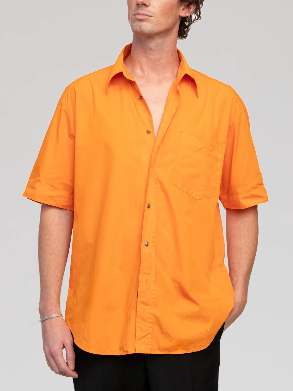 Vintage Versace Jeans Couture short-sleeve button-down shirt in a vibrant solid orange cotton poplin. Designed with a relaxed fit, spread collar, single chest patch pocket, cuffed short sleeves, metallic silver-tone front buttons, and a curved hemline. Made in Italy. - Image 1