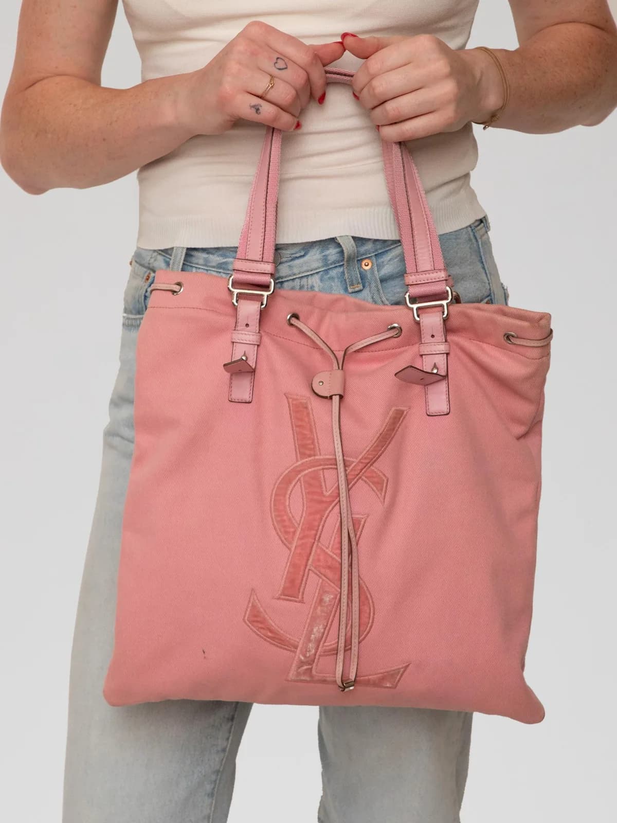 Crafted in soft dusty pink canvas, this vintage Yves Saint Laurent Rive Gauche Kahala tote bag features a prominent stitched leather YSL logo applique on the front, drawstring cinching, silver-tone hardware, and flat leather shoulder straps for a casual yet chic archival look. - Image 1